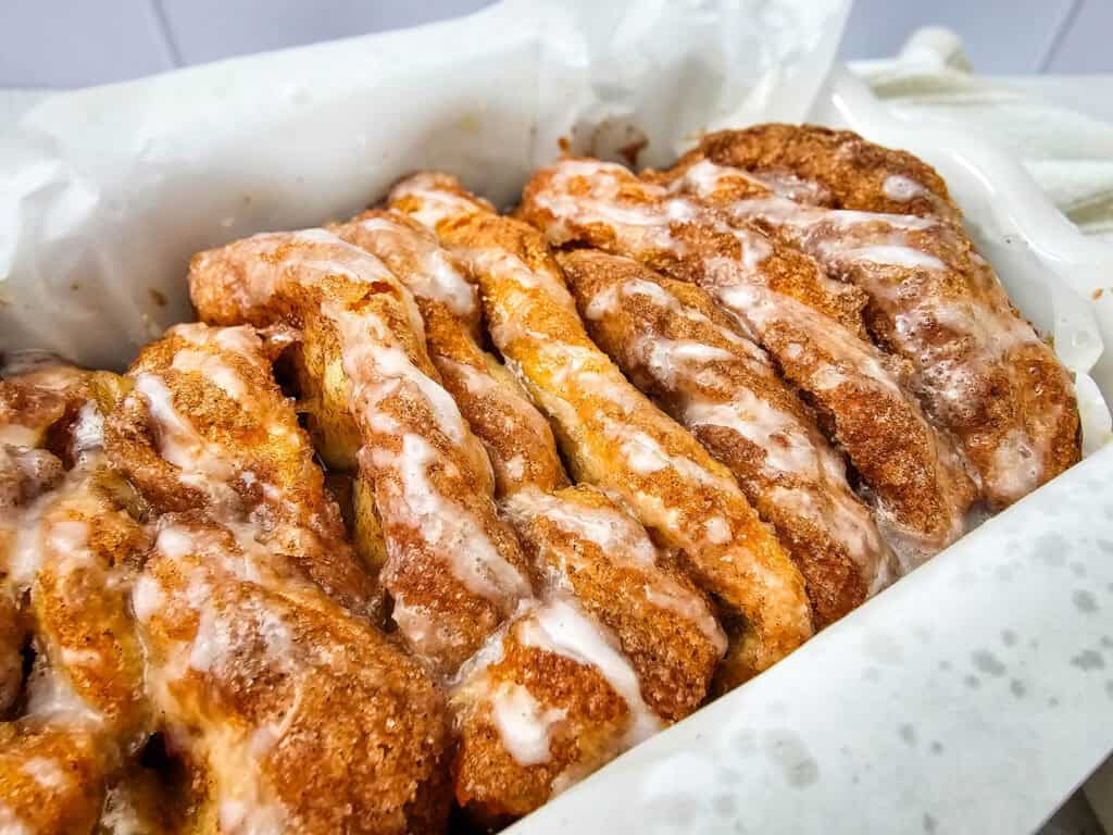 Close-up of freshly baked Apple Cinnamon Pull Apart Bread with a sugar glaze on top, arranged in a parchment-lined pan.