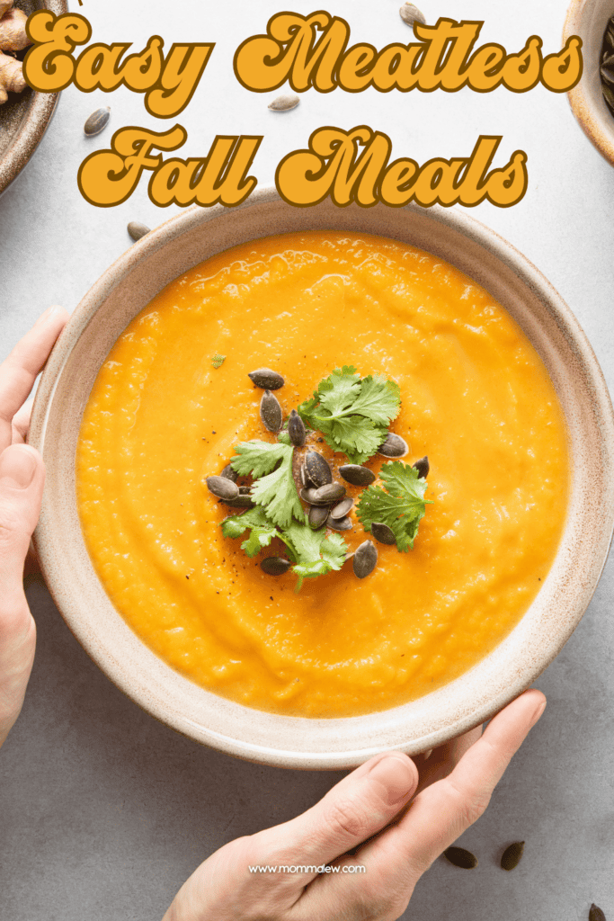 A bowl of creamy orange soup topped with cilantro and pumpkin seeds, with hands holding the bowl. The text on the image reads Easy Meatless Fall Meals, making it perfect for anyone looking for easy Fall dinner ideas.