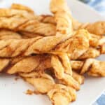 A white plate holds several golden brown Pumpkin Pie Twists with a cinnamon sugar coating, next to a blue and white striped cloth.